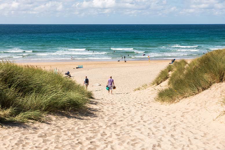 People walking through the sand dunes to the beach at Holywell Bay in North Cornwall