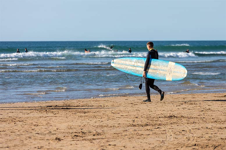 Someone walking towards the ocean at Perranporth holding a surf board